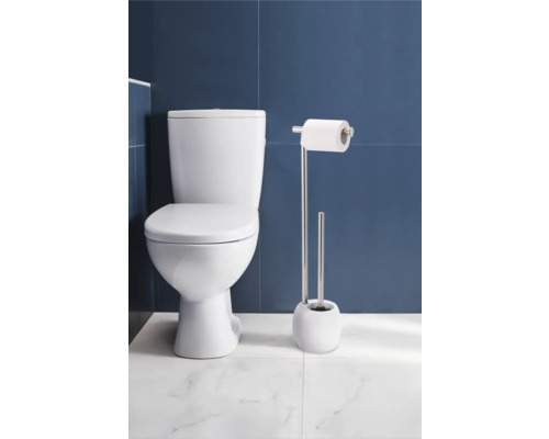 Toaletă de podea cu suport pentru hârtie igienică și set de perii WC în baie.