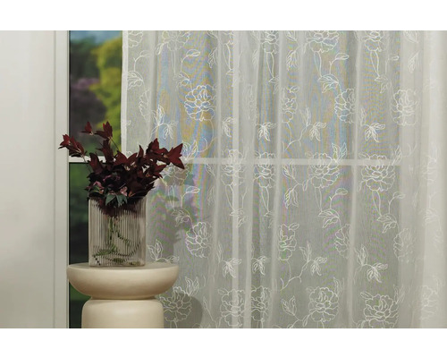 Cortină decorativă cu model floral în fața unei ferestre.