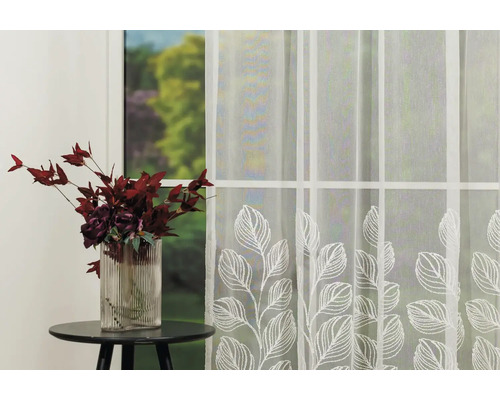 Fereastră decorativă cu perdea transparentă cu frunze și vază cu flori pe o masă