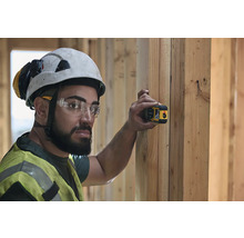 Un muncitor în construcții cu cască de protecție și vestă de siguranță folosește un dispozitiv de măsurare cu laser pe un perete de lemn.