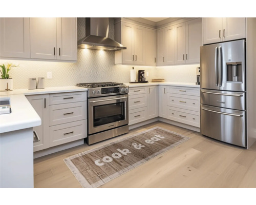 Bucătărie luminoasă cu dulapuri de bucătărie, hotă, aragaz, frigider și un covoraș cu inscripția Gătește și mănâncă