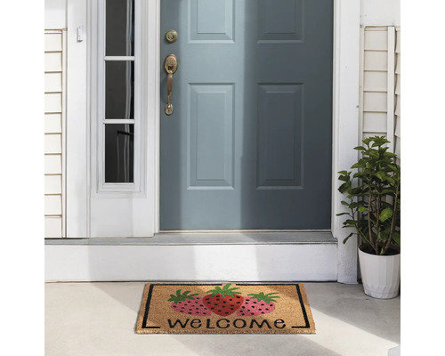 Covoraș de intrare cu motiv de căpșuni și inscripția Bine ați venit în fața unei uși de intrare