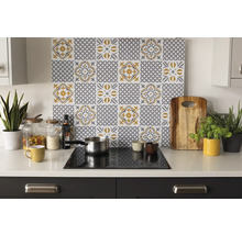 Bucătărie luminoasă și organizată cu un panou de protecție cu model de plăci gri-galben deasupra unui blat alb cu accesorii și plante.