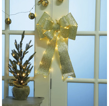 Arc decorativ auriu cu iluminare și brad mic în sac de iută pe masă în fața ușii