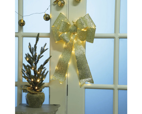 Arc decorativ auriu cu iluminare și brad mic în sac de iută pe masă în fața ușii