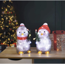 Două figurine de pinguin cu iluminare și motiv de Crăciun pe o masă în fața unui brad de Crăciun.