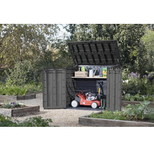 Dulap de grădină cu capac și ușă deschise în grădină, cu mașină de tuns iarba și unelte de grădinărit