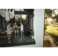 Trei bărbați ciocnesc pe terasă cu un grătar.