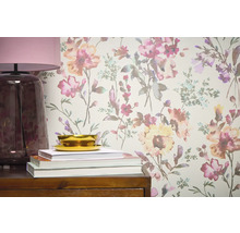 Prim-plan cu un perete cu tapet floral, completat de o lampă, cărți și un bol pe o piesă de mobilier din lemn.