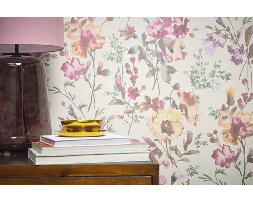 Prim-plan cu un perete cu tapet floral, completat de o lampă, cărți și un bol pe o piesă de mobilier din lemn.
