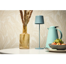 Natură statică decorativă cu lampă de masă, vază și termos pe fundalul unui tapet cu model.