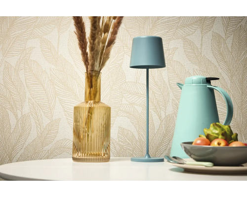 Natură statică decorativă cu lampă de masă, vază și termos pe fundalul unui tapet cu model.