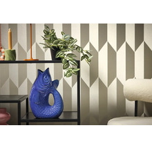 Interior decorativ cu raft, plantă și vază în formă de pește pe un fundal de tapet geometric.