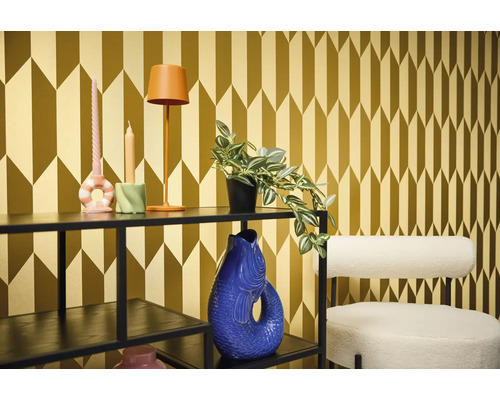 Cameră decorativă cu raft, lampă, lumânări, plantă, vază și scaun în fața unui tapet cu model