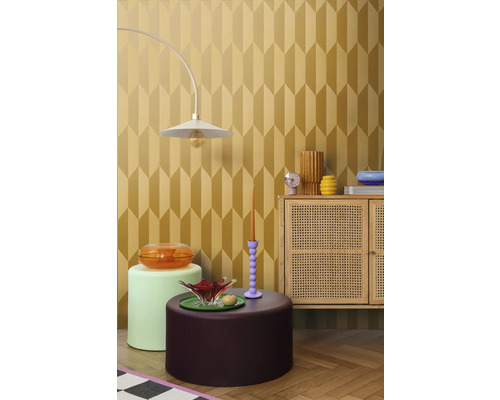 Exemplu de amenajare interioară cu o lampă, diverse mese și un dulap în fața unui tapet cu model geometric.