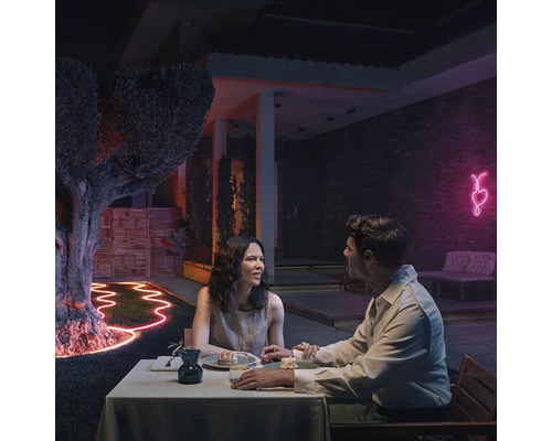 Un cuplu stă la o masă în grădină, iluminată cu un tub luminos flexibil