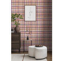 Interior de living cu tapet în carouri, comodă, taburet și decorațiuni pentru o atmosferă confortabilă.