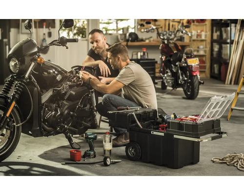 Doi bărbați repară o motocicletă cu o cutie de scule într-un garaj.