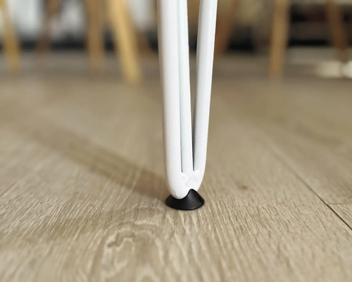 Prim-plan cu picior de masă alb cu protecție pentru podea pe o podea de lemn.