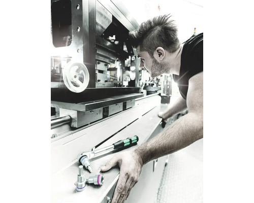 Un bărbat lucrează cu o cheie cu clichet la o mașină.