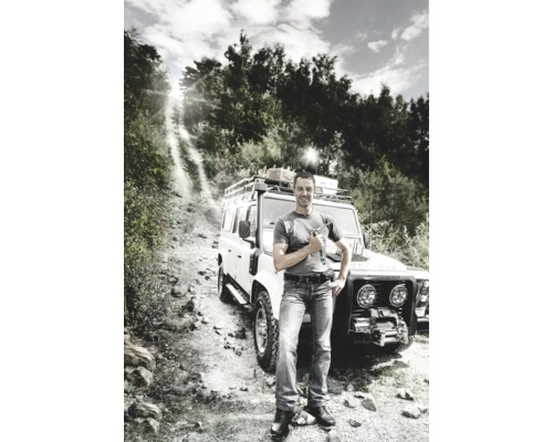 Bărbat cu șurubelniță în fața unui vehicul de teren pe un drum neasfaltat.