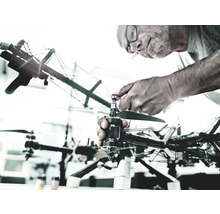 O persoană repară o dronă. Drona are mai multe elice și cablaje complexe.