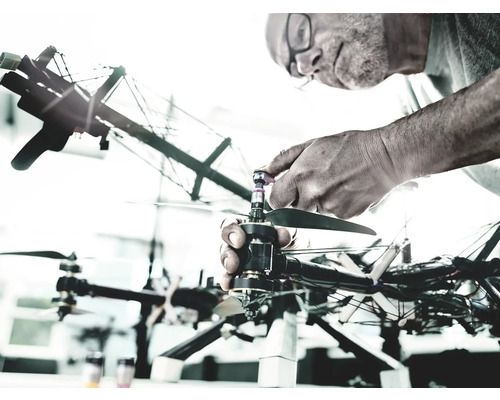 O persoană repară o dronă. Drona are mai multe elice și cablaje complexe.