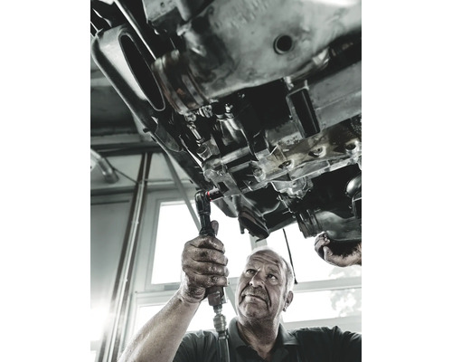 Un mecanic repară cutia de viteze a unei mașini cu o cheie cu clichet.