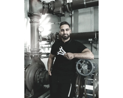 Un instalator cu chei stă în fața unei pompe industriale și a conductelor.