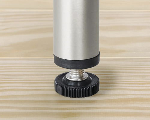 Imagine detaliată a unui picior de mobilier reglabil din metal și plastic pe o suprafață de lemn.