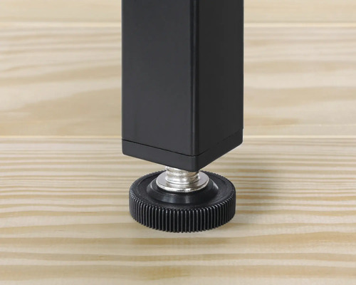 Prim-plan cu un picior de masă negru cu picior reglabil pe o podea de lemn.