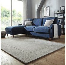 Cameră de zi cu canapea de colț albastră, perne decorative și covor dreptunghiular.