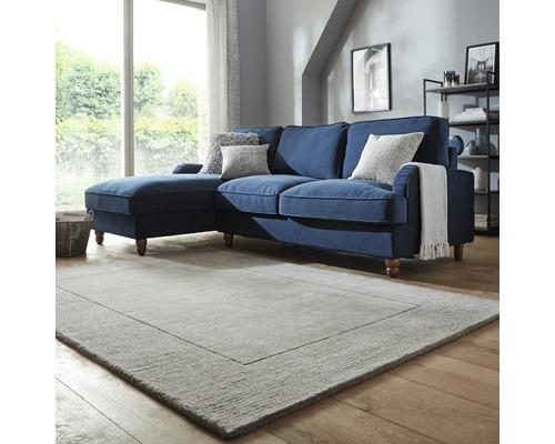 Cameră de zi cu canapea de colț albastră, perne decorative și covor dreptunghiular.