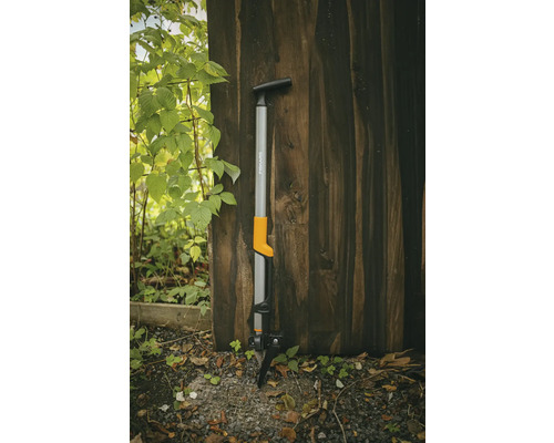 Extirpator Fiskars pentru buruieni, sprijinit de un perete de lemn