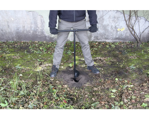 O persoană folosește un burghiu de pământ pentru a da o gaură în pământ.