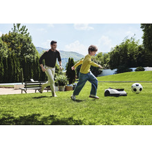 Bărbat și copil jucând fotbal cu robotul de tuns iarba în grădină.