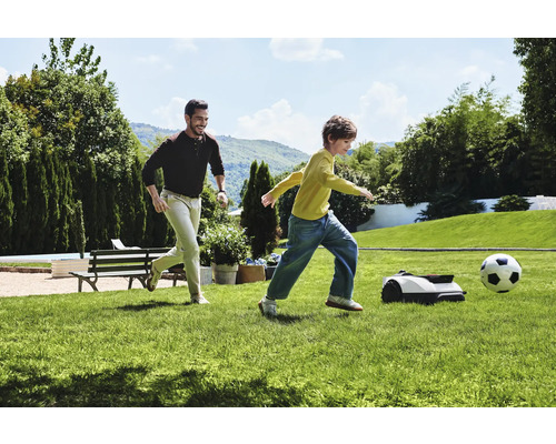 Bărbat și copil jucând fotbal cu robotul de tuns iarba în grădină.