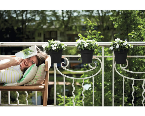 Femeie se relaxează cu o carte pe o bancă pe balcon cu jardiniere