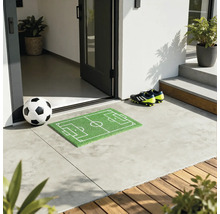 Mingie de fotbal în fața unei uși de intrare cu covoraș de fotbal și ghete de fotbal.