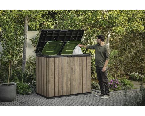 Box pentru pubele din lemn cu două pubele verzi și o persoană care aruncă un sac de gunoi înăuntru