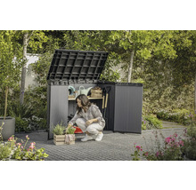 Grădină cu o femeie îngenuncheată în fața unui dulap de grădină deschis în care sunt depozitate unelte de grădină.