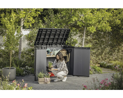 Scenă de grădină cu dulap de scule deschis în care o femeie depozitează unelte de grădinărit.