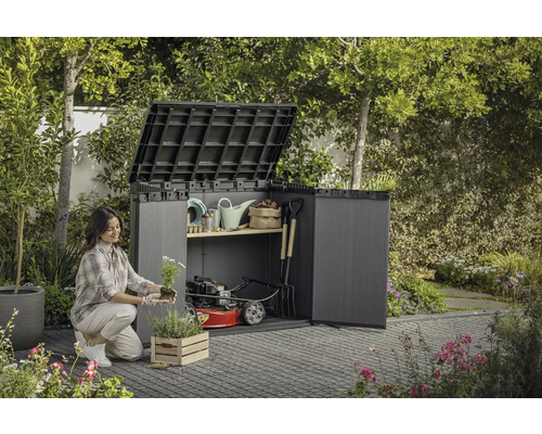 O femeie plantează flori în fața unui dulap de grădină deschis, cu unelte de grădinărit