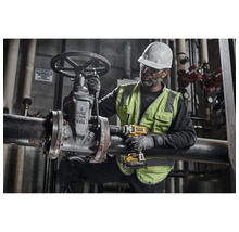 Un bărbat cu cască și vestă de protecție operează o supapă pe o conductă cu o cheie de impact cu acumulator.