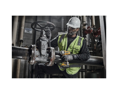 Un bărbat cu cască și vestă de protecție operează o supapă pe o conductă cu o cheie de impact cu acumulator.