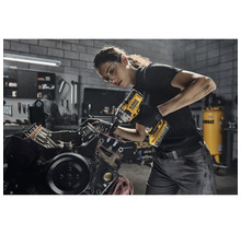 O femeie folosește o cheie de impact fără fir DeWalt pe un bloc motor într-un atelier.