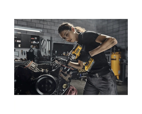 O femeie folosește o cheie de impact fără fir DeWalt pe un bloc motor într-un atelier.