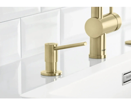 Dozator de săpun auriu lângă un robinet pe o chiuvetă.