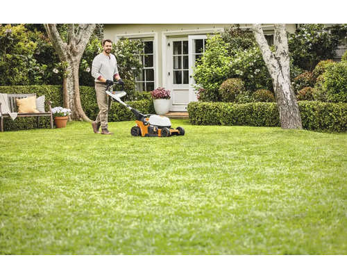 Bărbat tunde gazonul cu o mașină de tuns iarba în grădină
