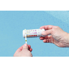 O persoană testează apa din piscină cu o bandă de testare și un kit de testare.